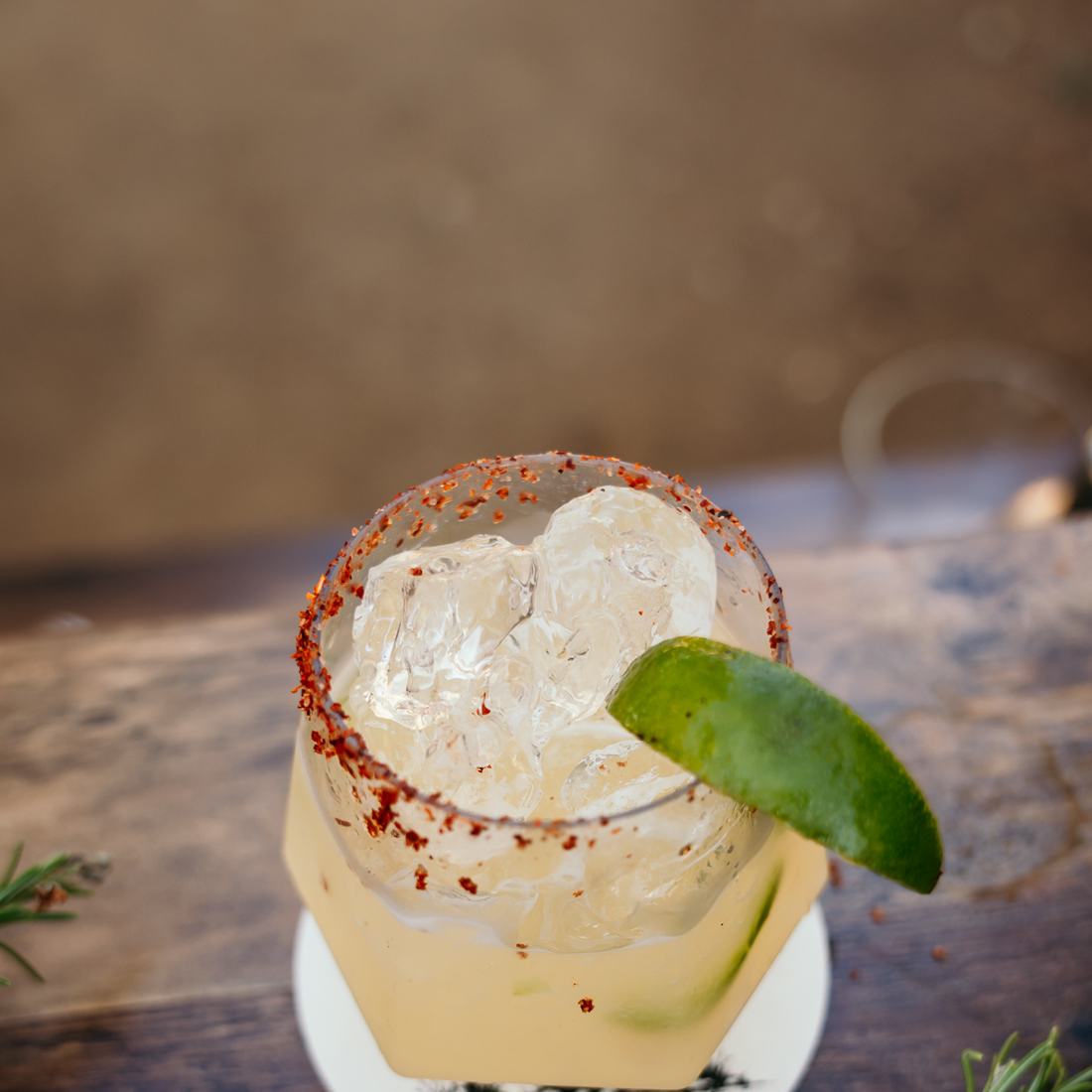 A spicy margarita with a chili-salt rim and a lime wedge on a wooden table